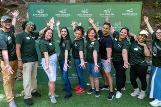 A cheerful group of people in green shirts poses together, smiling and showcasing a sense of community in front of a branded backdrop.