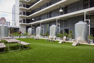 A vibrant outdoor space with artificial grass, picnic tables, and metal water tanks, surrounded by modern architecture and greenery.