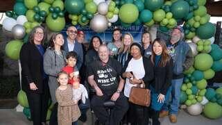 A diverse group of people poses together in front of a festive balloon backdrop, smiling and celebrating a special occasion.