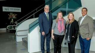 Four professionals stand together in a modern building, smiling near a staircase and a sign for EAH Housing.