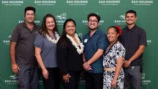 A group of six individuals poses together, smiling, in front of a green backdrop featuring EAH Housing branding.