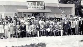 A large group poses in front of Nikkei Hall, showcasing a diverse community with men, women, and children, dressed in formal and casual attire.