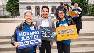 A group of activists holds signs advocating for housing justice and an end to homelessness, showcasing a united call for action.