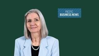 A woman with long gray hair, wearing a light blue jacket and pearl necklace, smiles against a green background featuring a logo for Pacific Business News.