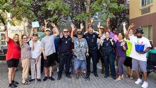 A diverse group of people and police officers gather outdoors, smiling and raising their hands in celebration or camaraderie.