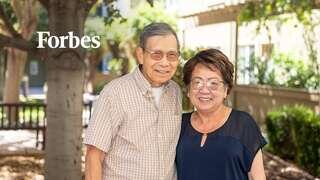 A smiling man and woman pose together outdoors, surrounded by greenery, showcasing a warm and cheerful moment.