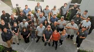 A diverse group of employees poses together, smiling and making gestures, showcasing team spirit and camaraderie in a casual setting.