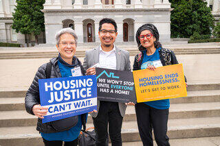 Three advocates hold signs promoting housing justice and the need to combat homelessness, standing in front of a government building in Sacramento, California.