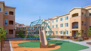 Avena Bella I features a colorful playground with a climbing structure and slide, surrounded by a modern affordable apartment community and landscaped greenery.