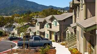 Drake’s Way Apartments, EAH Housing, exterior featuring modern two-story townhomes with flat roofs, neutral tones, and landscaped walkways with flowering trees and accessible pathways.