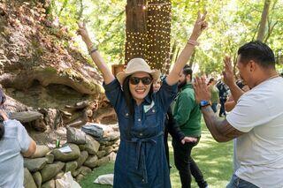 A joyful woman in a hat dances with raised arms, surrounded by friends smiling and celebrating in a lively outdoor setting.