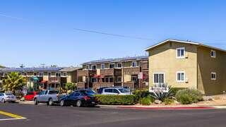Exterior view of Turina House, an EAH Housing apartment community with two-story buildings, balconies, rooftop solar panels, parked cars, and a playground in the foreground.
