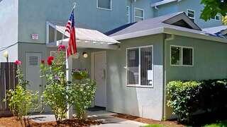 Exterior view of Riverfield Homes, a residential community featuring small homes with landscaped yards and an American flag at the entrance.