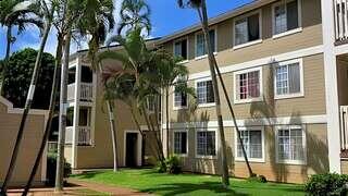 Hibiscus Hill features a three story affordable housing community by EAH Housing with light siding, red accents, and landscaped greenery with palm trees