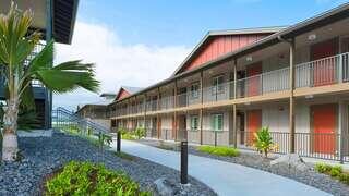 Hale Nā Koa ‘O Hanakahi features a two story affordable housing community by EAH Housing with open air walkways, red doors, and tropical landscaping in a lush Hawai‘i setting