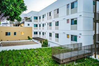 Modern multi-story buildings with a mix of white and beige exteriors, greenery, and a deck area, creating a welcoming urban environment.