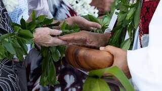Hands exchange a wooden bowl and green leaves, symbolizing unity and tradition during a ceremonial moment.