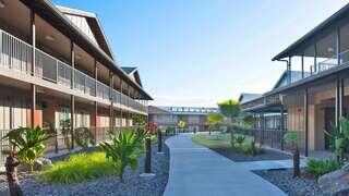 A modern courtyard with two-story buildings, landscaped plants, and a winding pathway under a clear blue sky.