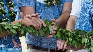 Hands adorned in vibrant attire hold a braided green lei, symbolizing connection and tradition. A cultural gathering captured in unity.