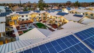 Aerial view of a modern apartment complex with solar panels on rooftops, green spaces, and pathways, showcasing sustainable living.