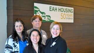 Four professionals pose together in front of a sign celebrating 50 years of service for EAH Housing, smiling and engaged.