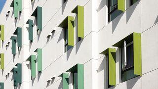 A modern building façade features a pattern of white walls and green accents around the windows, creating a vibrant and geometric appearance.