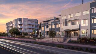 Modern residential buildings line a street, with trees and a vibrant sunset sky in the background, creating a welcoming atmosphere.