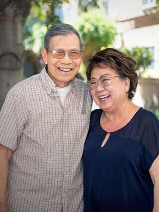 Two smiling older residents, stand close together, enjoying a joyful moment outdoors in the sunlight. They share a warm and friendly connection.