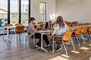 Future residents sign leasing paperwork in the Greenfield Commons community room, a bright, modern space with large windows and orange chairs.