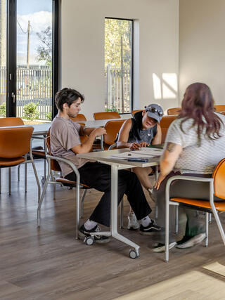 Future residents sign leasing paperwork in the Greenfield Commons community room, a bright, modern space with large windows and orange chairs.
