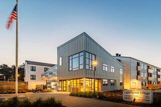 A modern building with large windows and a unique architectural design, surrounded by landscaping, lights, and an American flag.