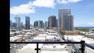 A vibrant Honolulu skyline features modern skyscrapers with a blue sky and ocean view, showcasing a bustling urban landscape below.