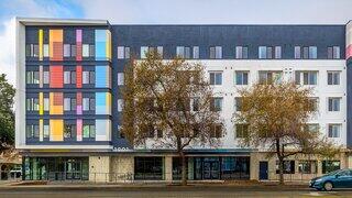 A modern building features a colorful façade alongside a minimalist design, framed by bare trees and a clear sky.