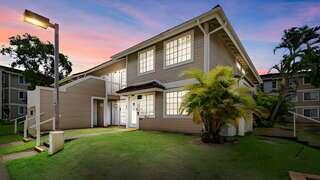 A charming two-story building in a tropical setting, featuring large windows and landscaping, with a colorful sunset in the background.