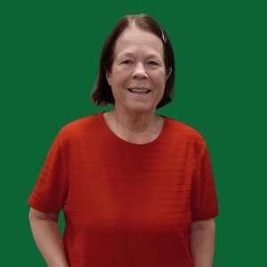 A smiling woman with shoulder-length brown hair wears a bright red shirt against a green background. Her cheerful demeanor is welcoming.