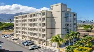 A modern, multi-story building surrounded by palm trees, with a parking lot and mountains in the background under a clear blue sky.