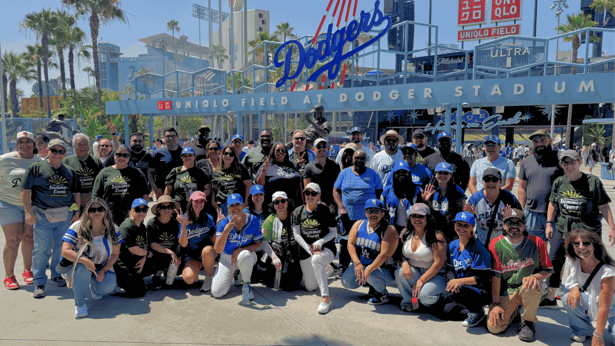 A large group of people in team apparel poses happily outside Dodger Stadium, showcasing excitement and camaraderie during a game day.
