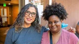 Two women smile together, one wearing a shirt promoting a nonprofit focused on ending homelessness, highlighting community support and connection.