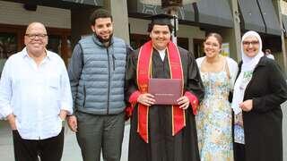 A proud graduate stands with family members, all smiling, celebrating a significant achievement in front of a venue.