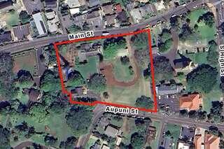 An outlined parcel of land at the intersection of Main St and Aupuni St, surrounded by various structures and greenery.