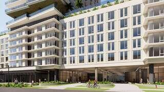 A modern multi-story building features large windows, balconies, and green landscaping, with pedestrians and cyclists nearby.