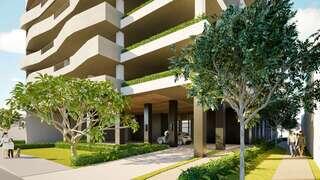 A modern building features curved balconies, lush greenery, and a spacious entrance with trees lining the sidewalk and people walking by.