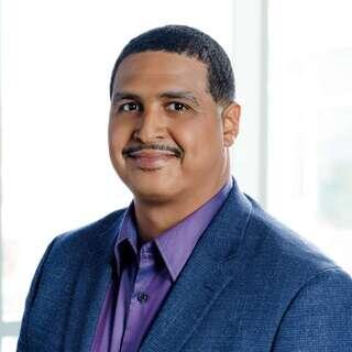 Welton Jordan, Chief Real Estate Officer at EAH Housing, smiling in a navy blazer and purple shirt.