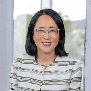 Junhee Byun, Vice President of Accounting at EAH Housing, smiling in a striped white and olive jacket with glasses.