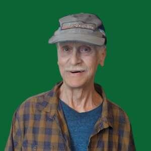 An older man with a friendly smile wears a cap and a plaid shirt, set against a solid green background.