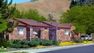 Del Ganado features affordable housing by EAH Housing with single story residences, wood shingle siding, landscaped greenery, and a hillside backdrop in a quiet neighborhood.