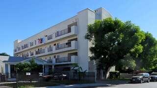 A multi-story apartment building with balconies, featuring clothes hanging out to dry, surrounded by trees and parked cars.