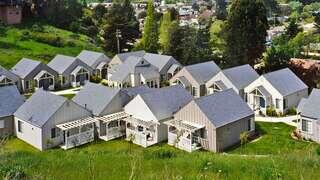 A quaint cluster of modern homes with gray roofs is nestled in a lush, green landscape, surrounded by trees and a serene atmosphere.