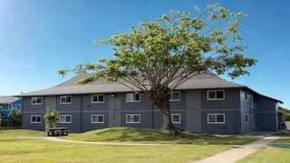 A spacious gray building surrounded by a green lawn features a large tree, creating a tranquil outdoor setting with a picnic area.