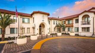 Exterior shot of Willow Housing, beige color 2 floor adobe style apartments with prominent tree next to building